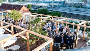 Terraza en la azotea con barandillas de madera, mobiliario exterior y vistas a la ciudad y vías de tren.