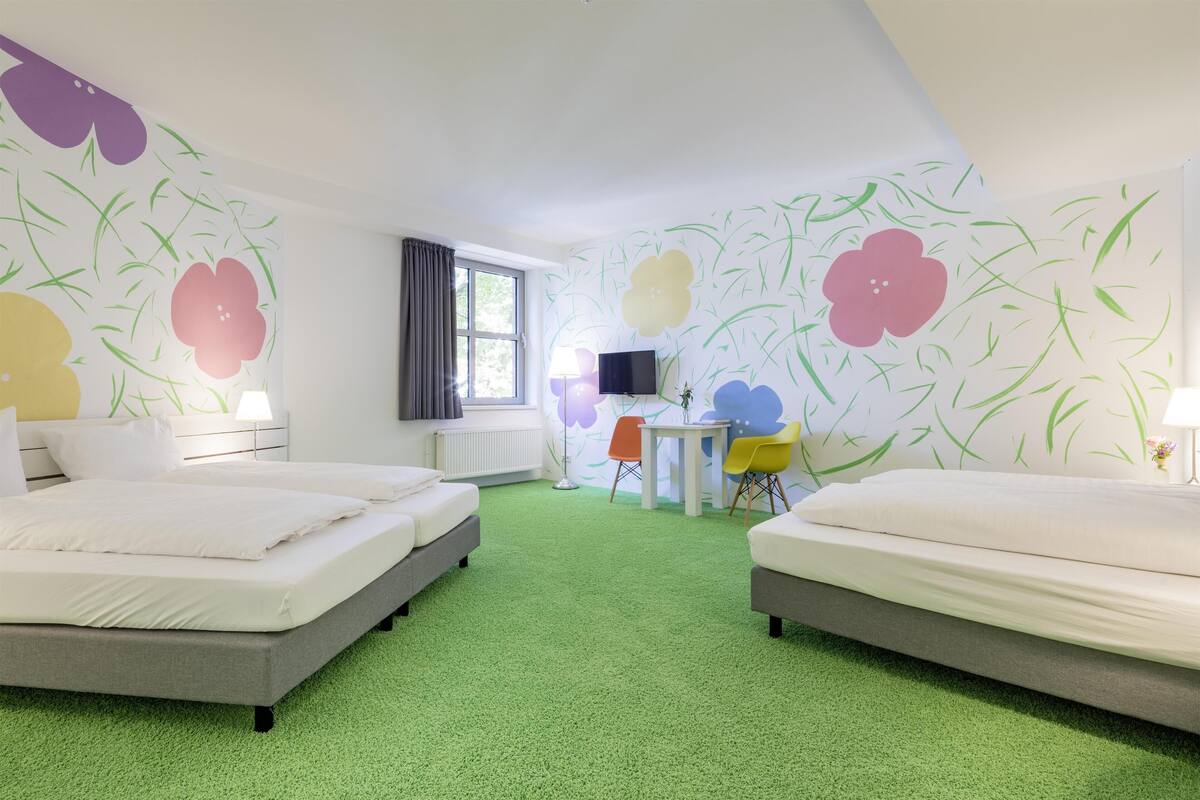 Ein Hotelzimmer mit zwei Betten, einem Fernseher, einem kleinen Tisch und Stühlen.