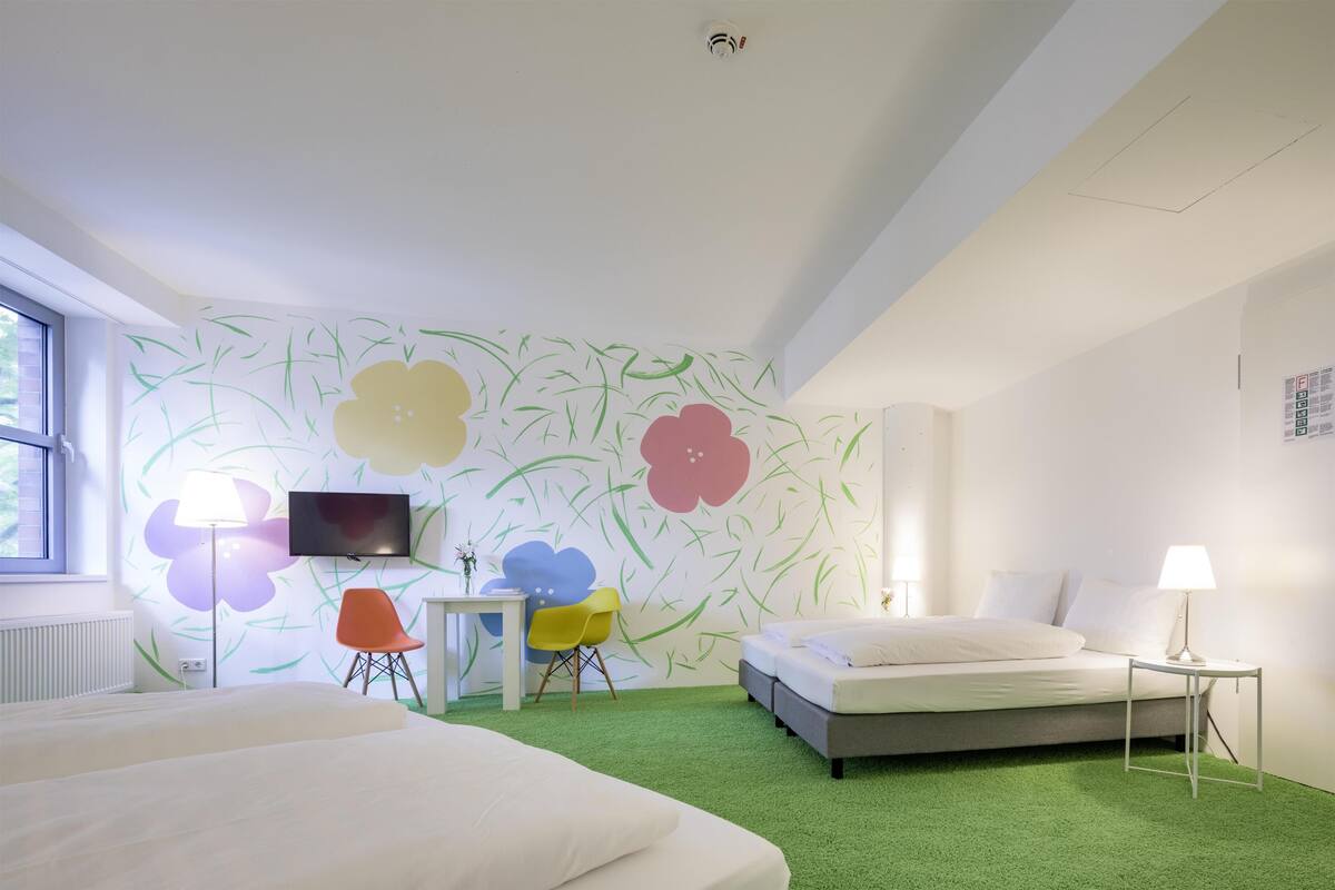 Ein modernes Hotelzimmer mit grünem Teppich, einem Bett, einem Schreibtisch mit Stuhl, einem Fernseher und einem Fenster.
