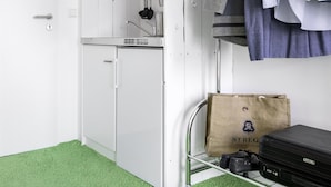 Una habitación pequeña con kitchenette, un perchero y una maleta en el suelo.