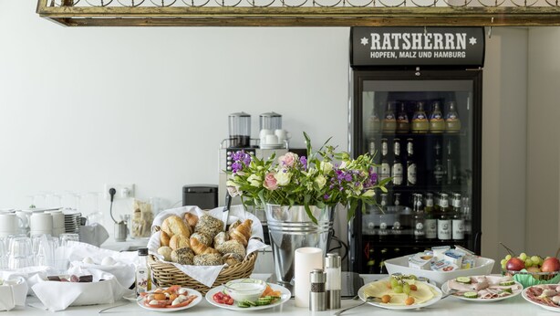 Un bufé de desayuno con diversas opciones de alimentos, un dispensador de bebidas y un jarrón decorativo con flores.
