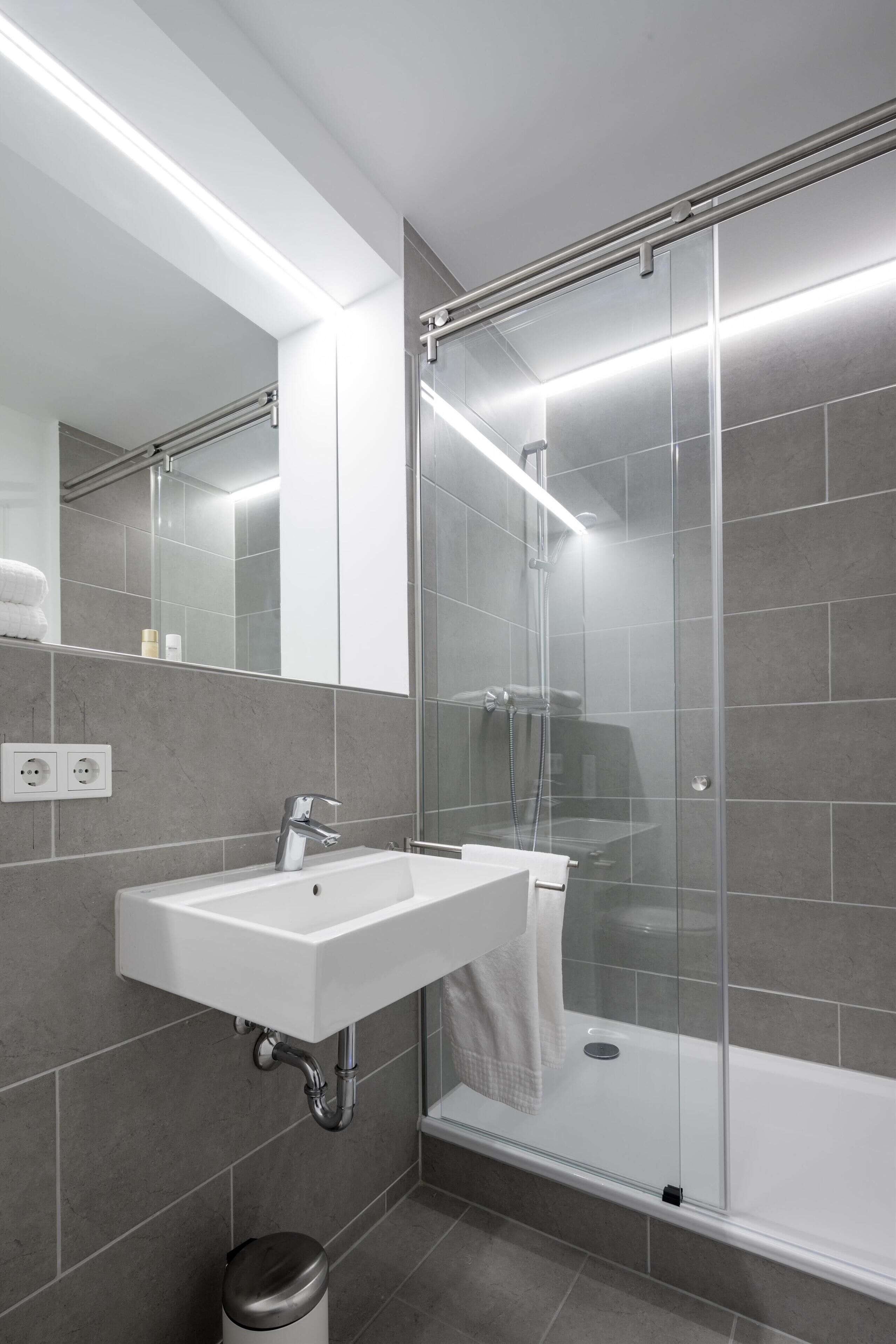 Casa de banho moderna com lavatório branco, espelho e cabine de duche em vidro.