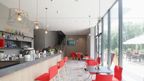 Un área de bar moderna con sillas rojas, una barra con diversas botellas y un ventanal que ofrece vistas al exterior.
