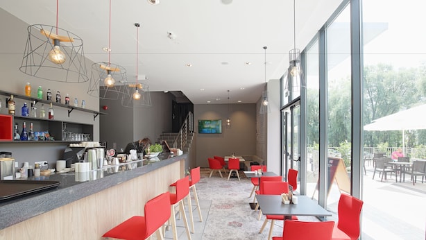 Un área de bar moderna con sillas rojas, una barra con diversas botellas y un ventanal que ofrece vistas al exterior.