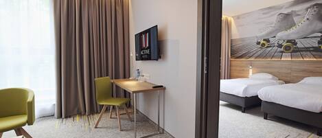 Habitación de hotel con cama, escritorio, dos sillas, televisor y un mural de patines en la pared.