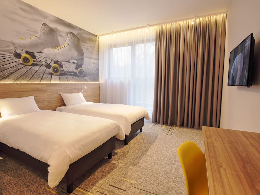 A hotel room with two beds, a wooden headboard, a large TV, and a window with curtains.
