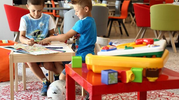 Dos niños dibujando en una mesa, con bloques de construcción de colores cerca.