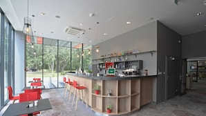 Zona de bar moderna con una barra curva, sillas rojas y vistas a zonas verdes.