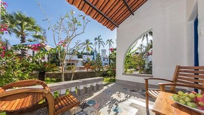 Un patio con suelo de baldosas, mobiliario de madera y vistas del entorno, incluyendo palmeras y edificios.