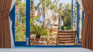 Una habitación con vistas a un jardín, una silla de madera y una mesa con fruta.