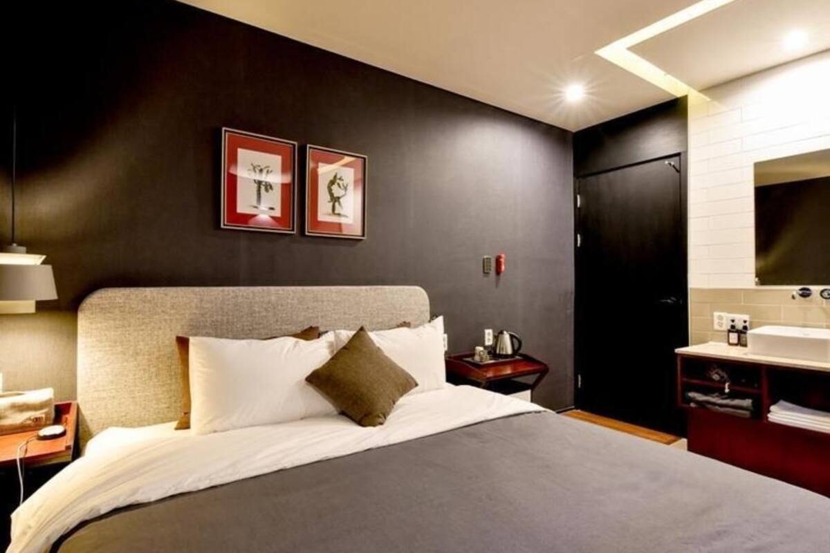A modern hotel room with a large bed, bedside table, and a dark wall with two framed pictures.
