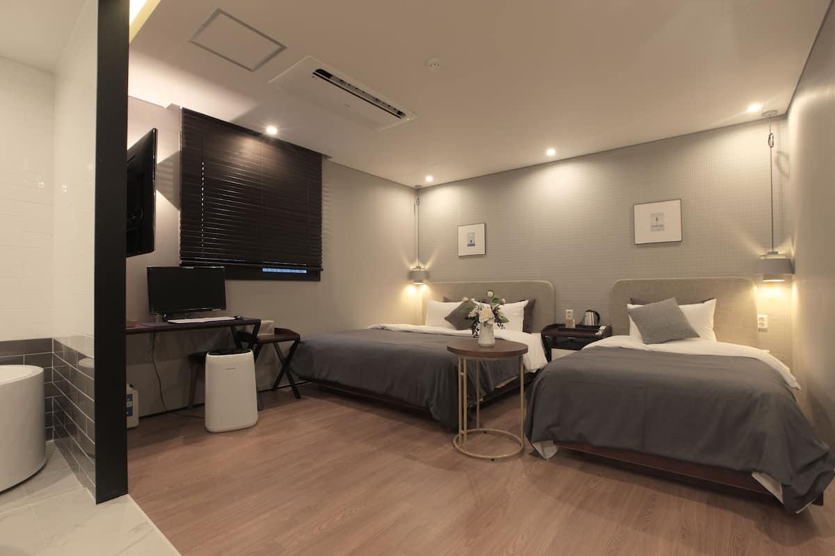 A modern hotel room with two beds, a desk, and a television.