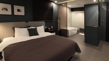 A modern bedroom with a large bed, a bedside table, a nightstand, a built-in shower, and a glass partition.