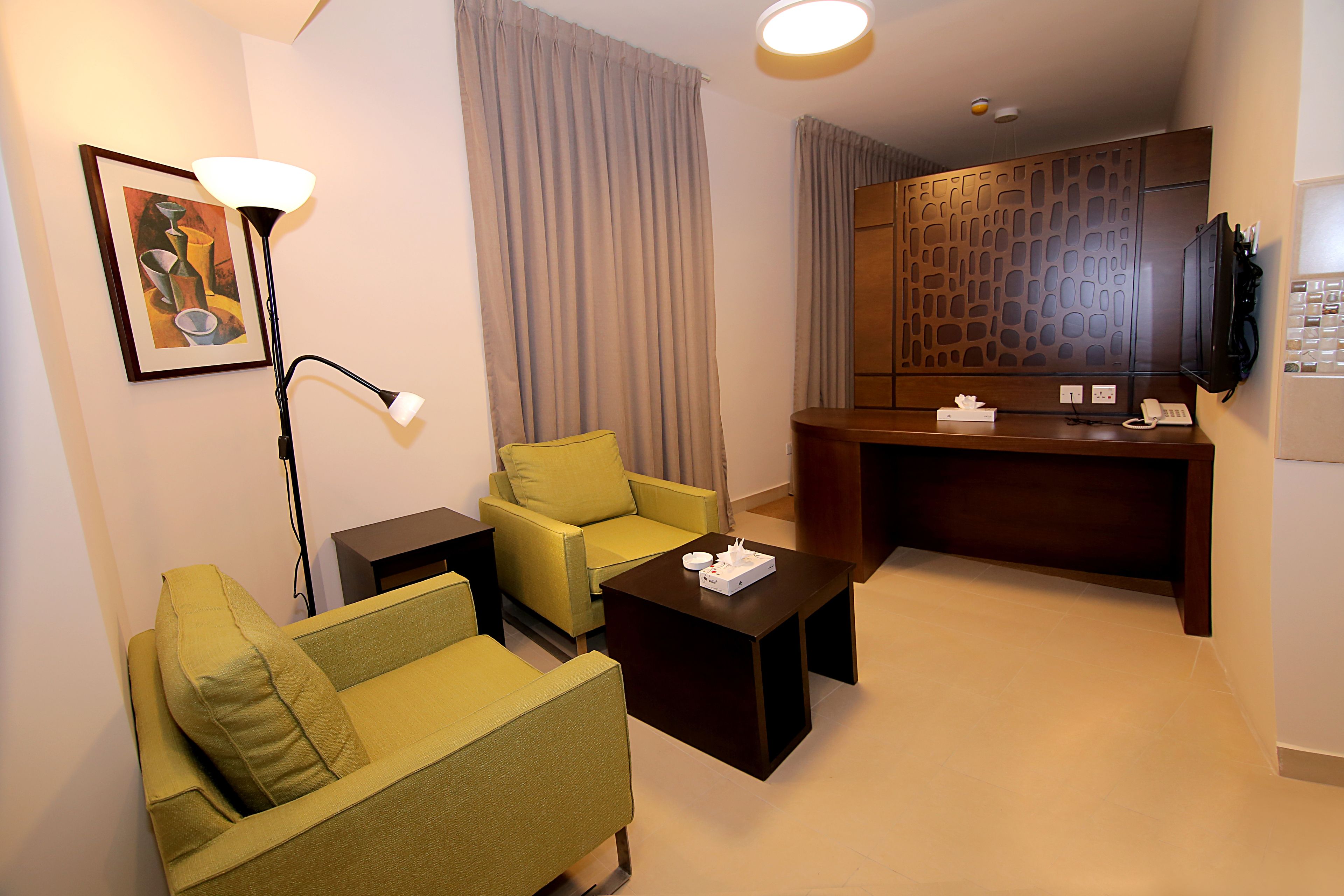 Habitación de hotel con sofá verde, una mesita de centro pequeña, escritorio con teléfono y televisor.