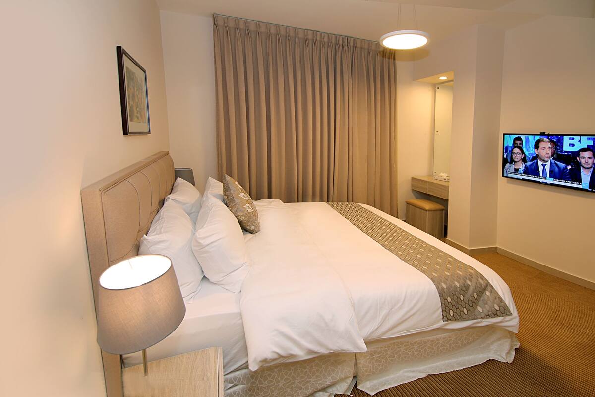 A hotel room with a bed, a TV, a lamp, and a large window with curtains.