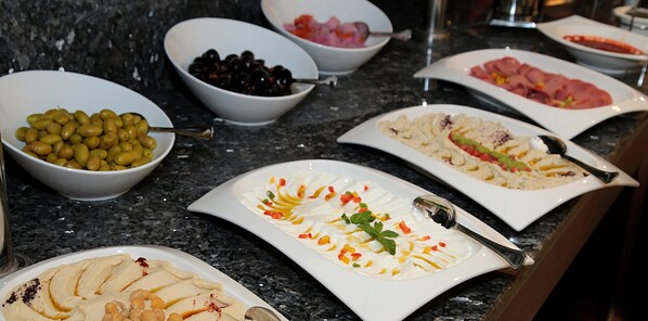 A buffet table with various dishes including olives, hummus, and a salad.