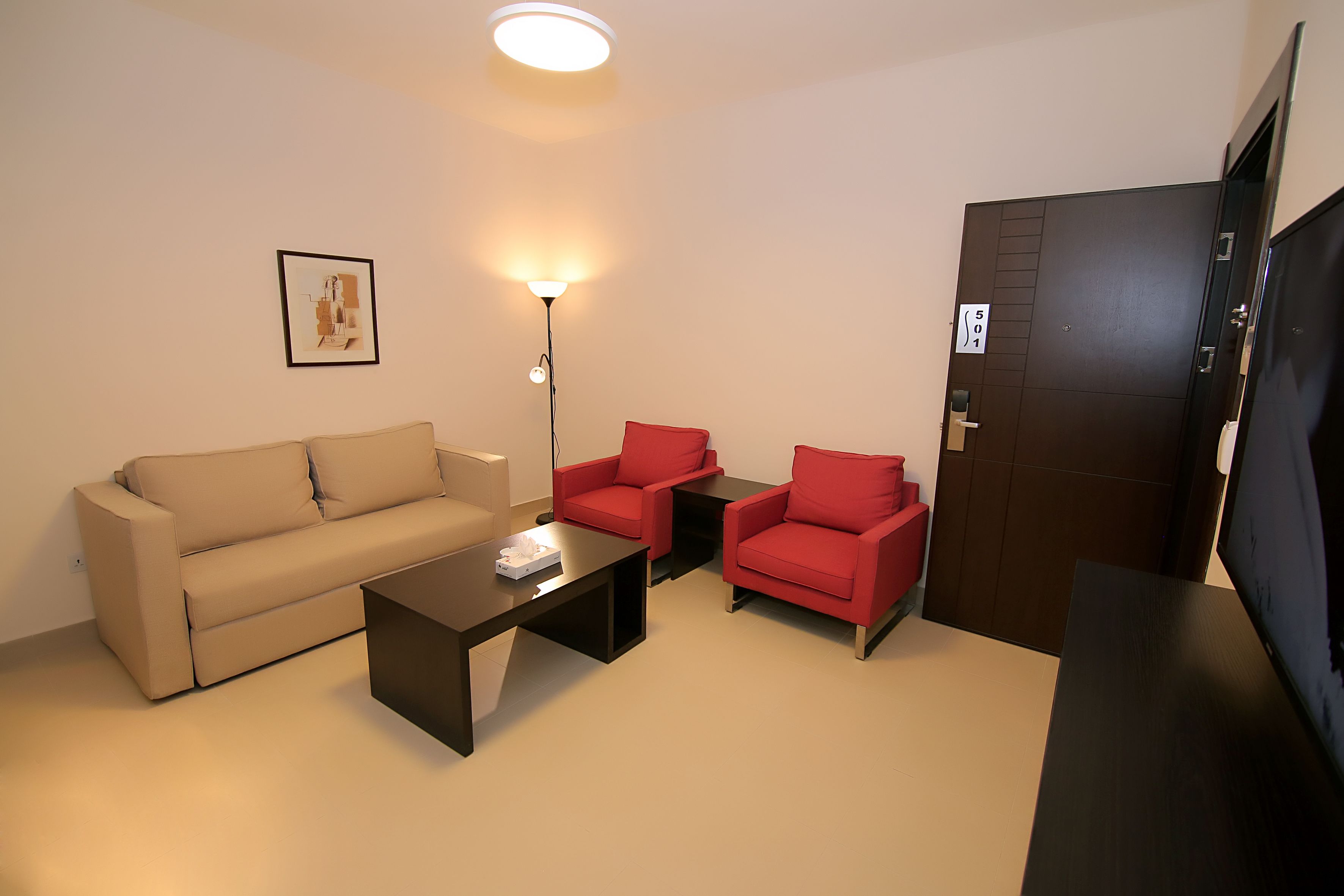 Ein Wohnzimmer mit einer Couch, zwei roten Sesseln, einem Couchtisch, einer Stehlampe und einem Fernseher.