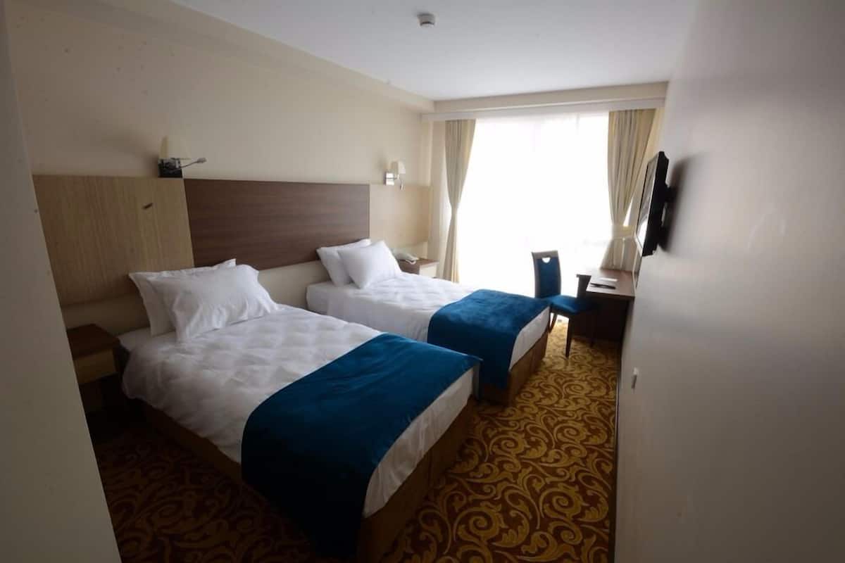A hotel room with two beds, a desk, a chair, a TV, and a window with curtains.