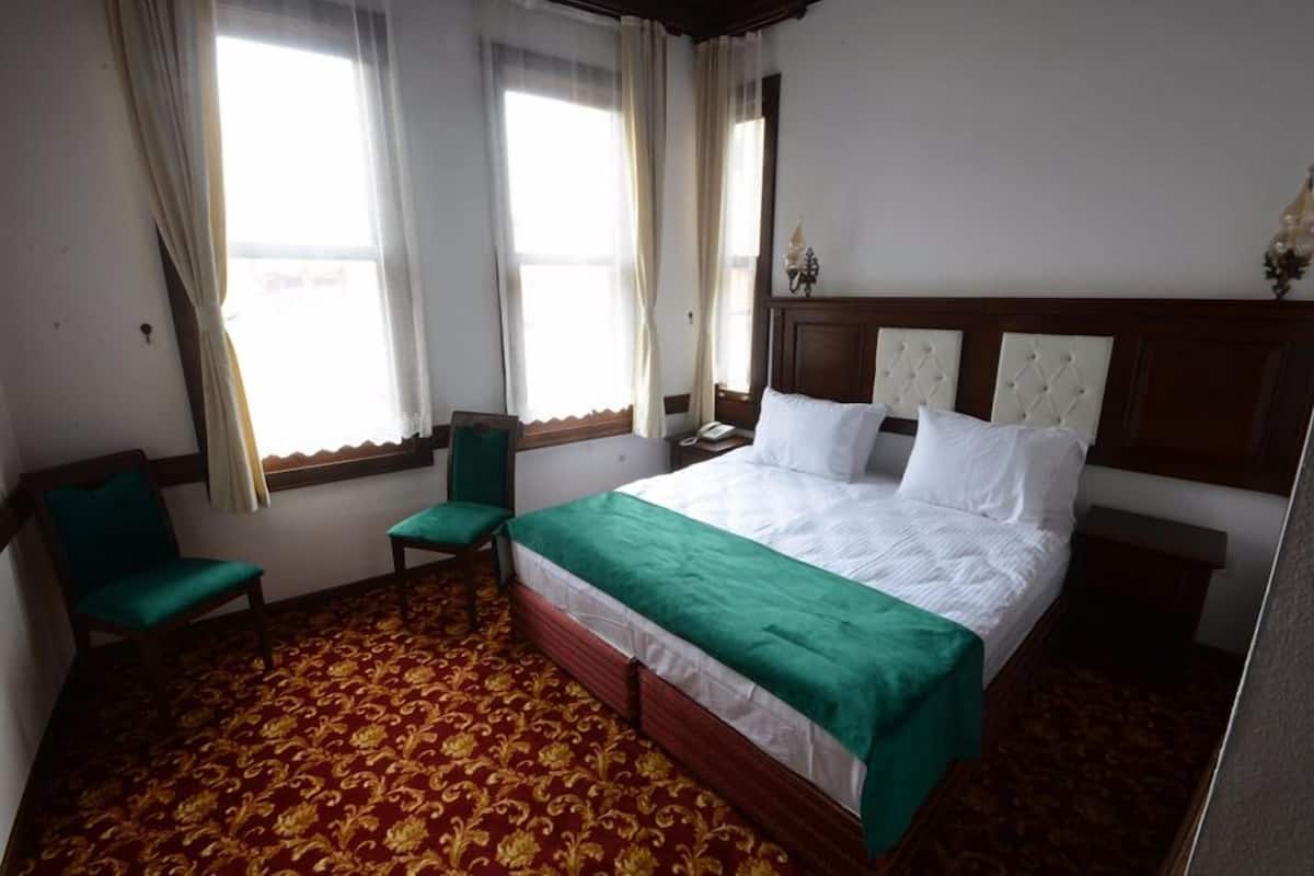 A hotel room with a large bed, a green chair, a small table, and a window with curtains.