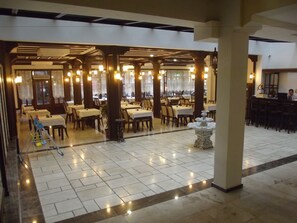 Ein geräumiges Restaurant mit mehreren Tischen und Stühlen, einer zentralen Fontäne und freundlicher Beleuchtung.