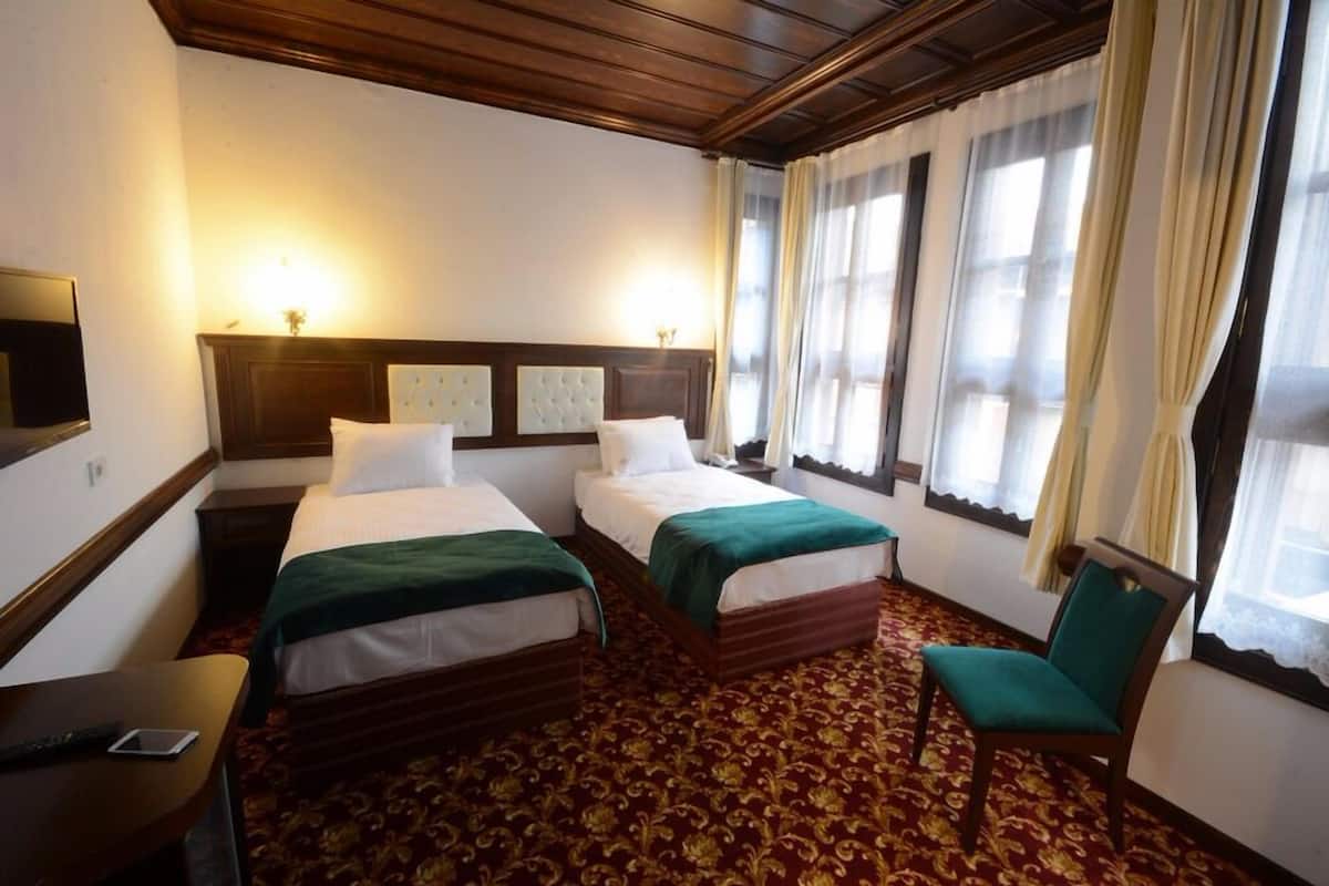 A hotel room with two beds, a chair, a desk with a phone, and a large window with curtains.