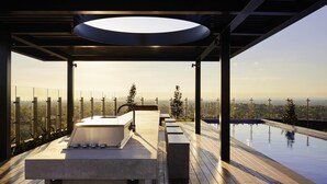 Un baño exterior moderno con una bañera independiente, un tragaluz circular grande y vistas a un paisaje urbano.
