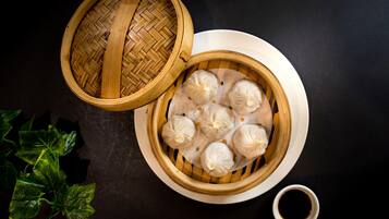 A bamboo steamer with dumplings on a white plate, accompanied by a small bowl of soy sauce.