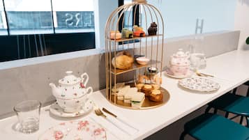 Une table dressée avec une théière, des tasses, des assiettes et un présentoir à étages contenant des pâtisseries et des sandwichs.
