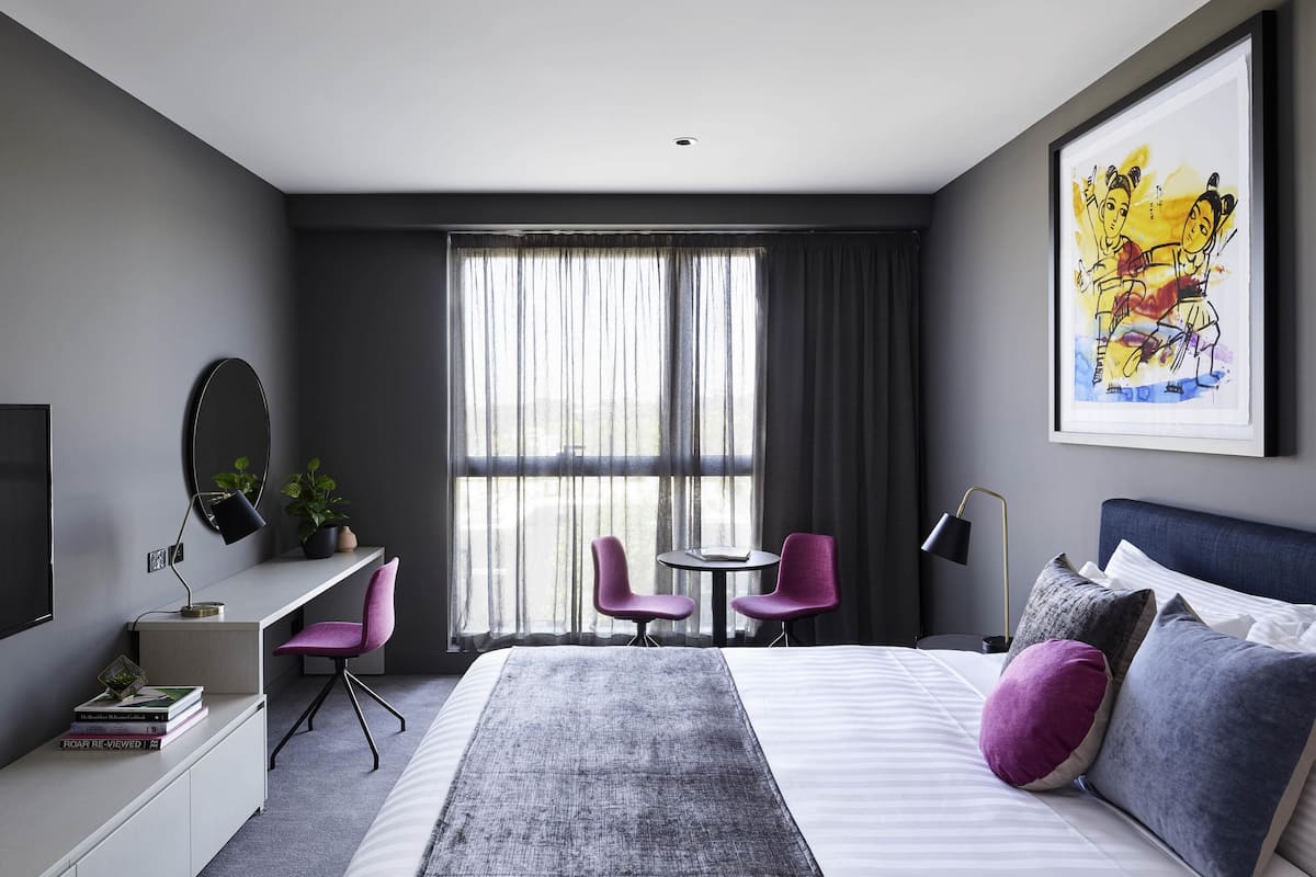 Een moderne hotelkamer met een bed, bureau, stoelen en een groot raam.