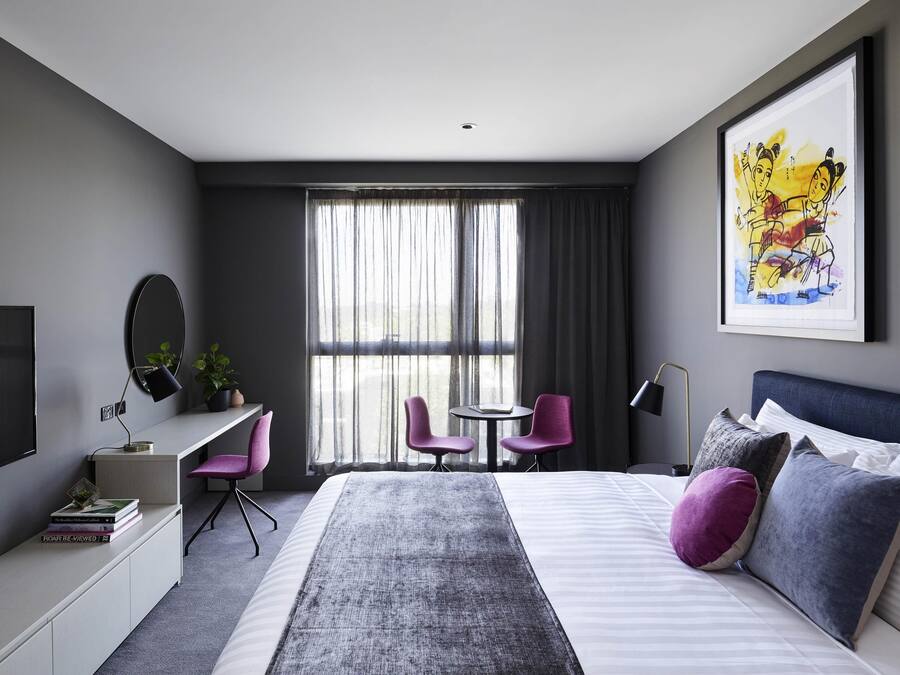 Ein modernes Hotelzimmer mit Bett, Schreibtisch, Stühlen und einem großen Fenster.