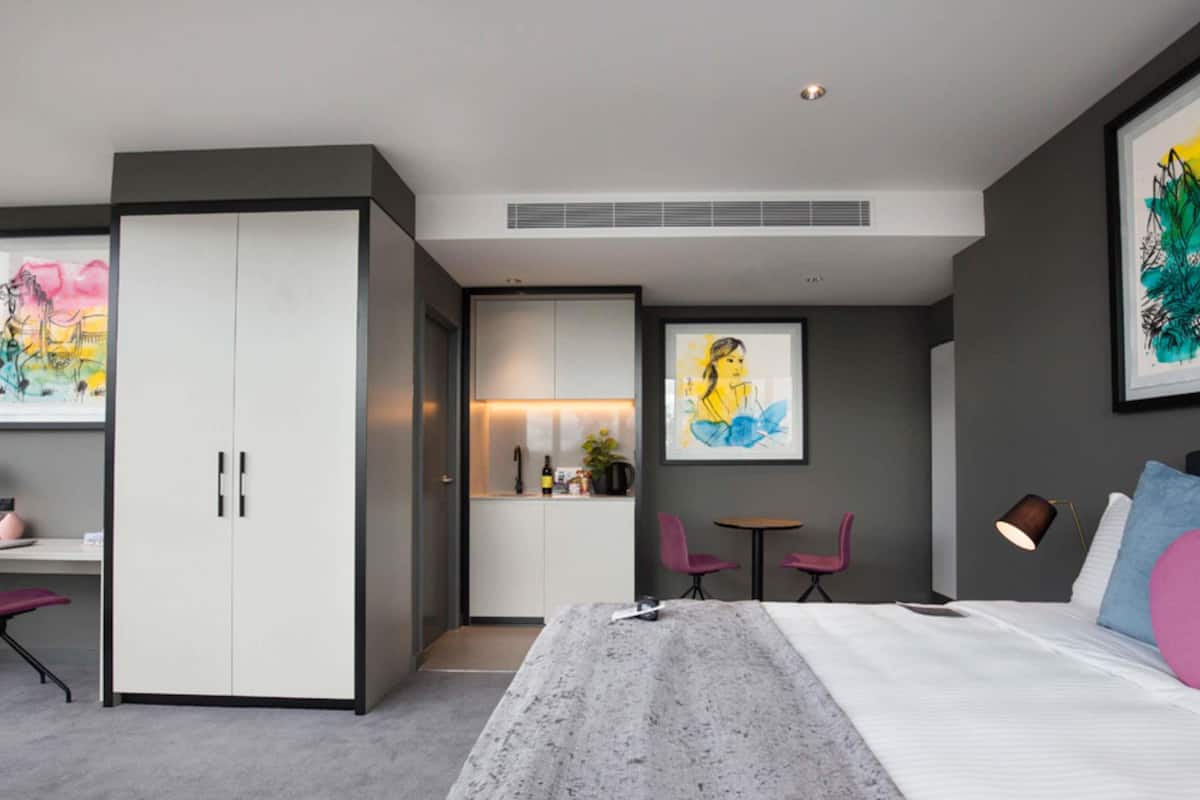 Een moderne slaapkamer met een bed, een bureau, een kledingkast en een klein zithoekje.