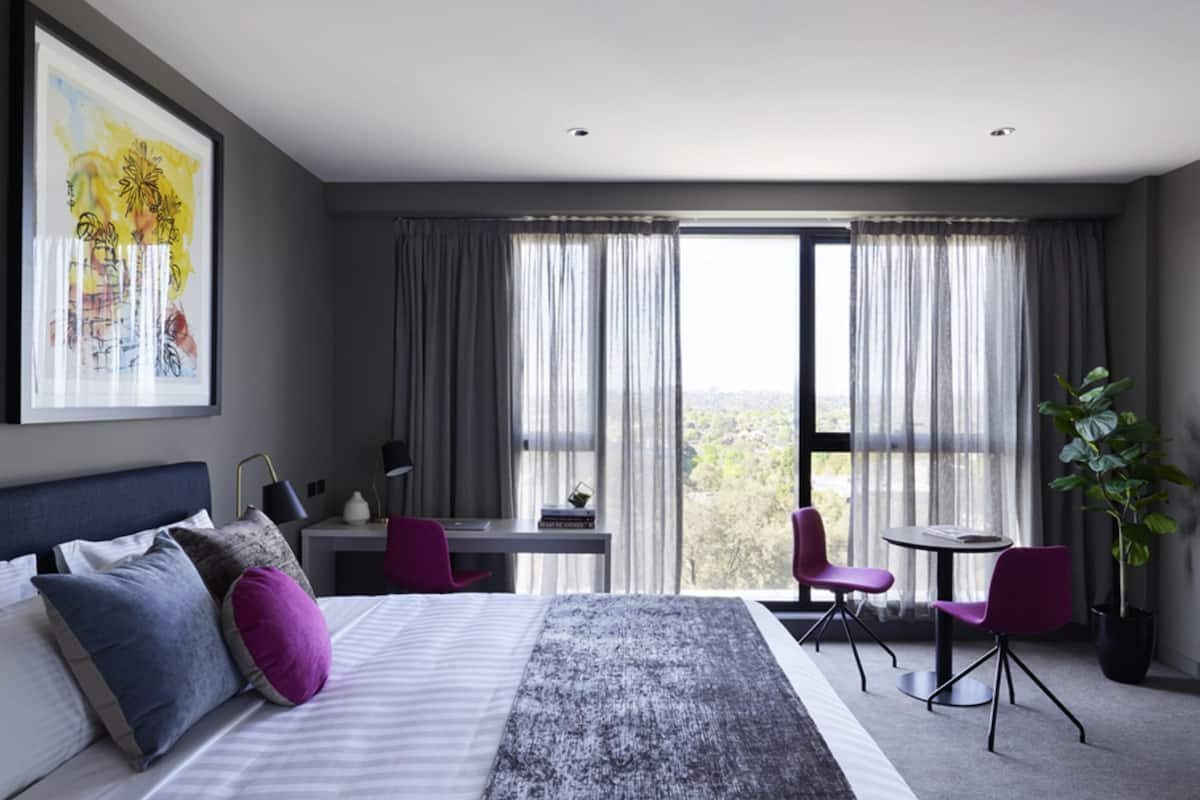 Een moderne hotelkamer met een groot bed, een bureau, twee stoelen, een potplant en uitzicht op de stad.