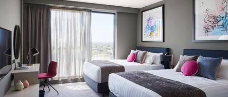 A hotel room with two beds, a desk, a chair, and large windows with curtains.
