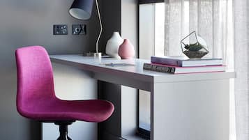 Una taula moderna amb una cadira rosa, una làmpada i objectes decoratius com llibres i un terrari de vidre.
