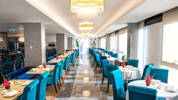 Un restaurante con filas de sillas y mesas tapizadas en azul, un candelabro y una zona de bar al fondo.