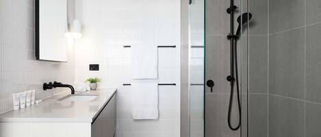 Un baño moderno con cabina de ducha de vidrio, paredes de azulejos blancos, encimera blanca y un espejo.