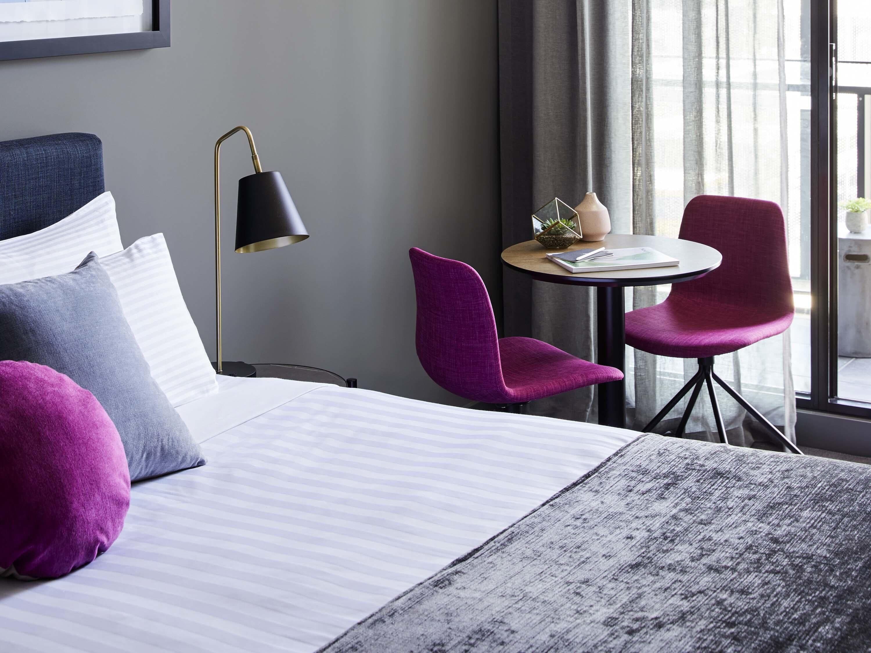 Une chambre d’hôtel avec un lit, un bureau, deux chaises, une lampe et une vue sur l’extérieur.