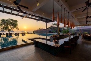 Een poolbar met uitzicht op de ondergaande zon, terrasstoelen en een zwembad.