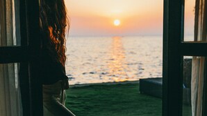 A person leaning out of a window overlooking a sunset over water. -  Regenta Arie Lagoon Negombo (Negombo)