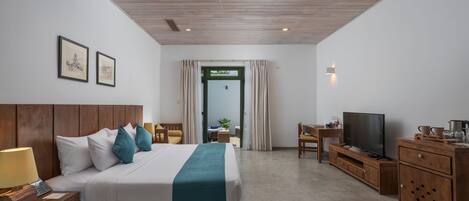 Habitación de hotel con cabecera de madera, cama con ropa de cama blanca y turquesa, mesita de noche con lámpara, televisor sobre un mueble de madera, y vistas al exterior a través de una puerta.
