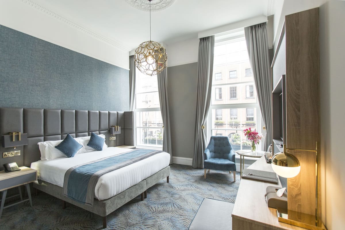 Una habitación de hotel con una cama grande, un escritorio, una silla y una ventana con cortinas.