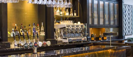 Una zona de bar con mostrador, taburetes y una variedad de botellas y vasos.