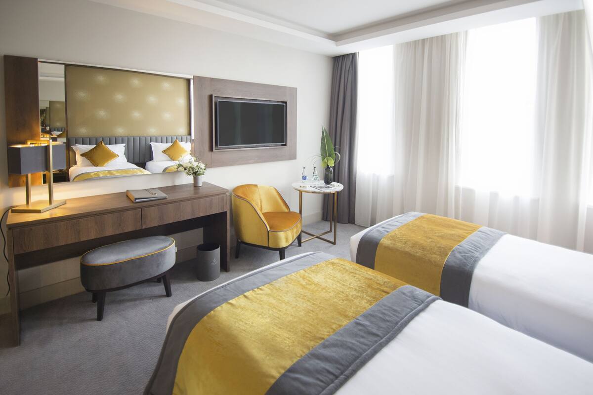 Habitación de hotel con cama, escritorio, silla, televisor y ventana con cortinas.