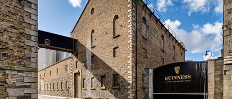 A historic building with a stone facade, a large black gate with the Guinness logo, and a cobblestone street.