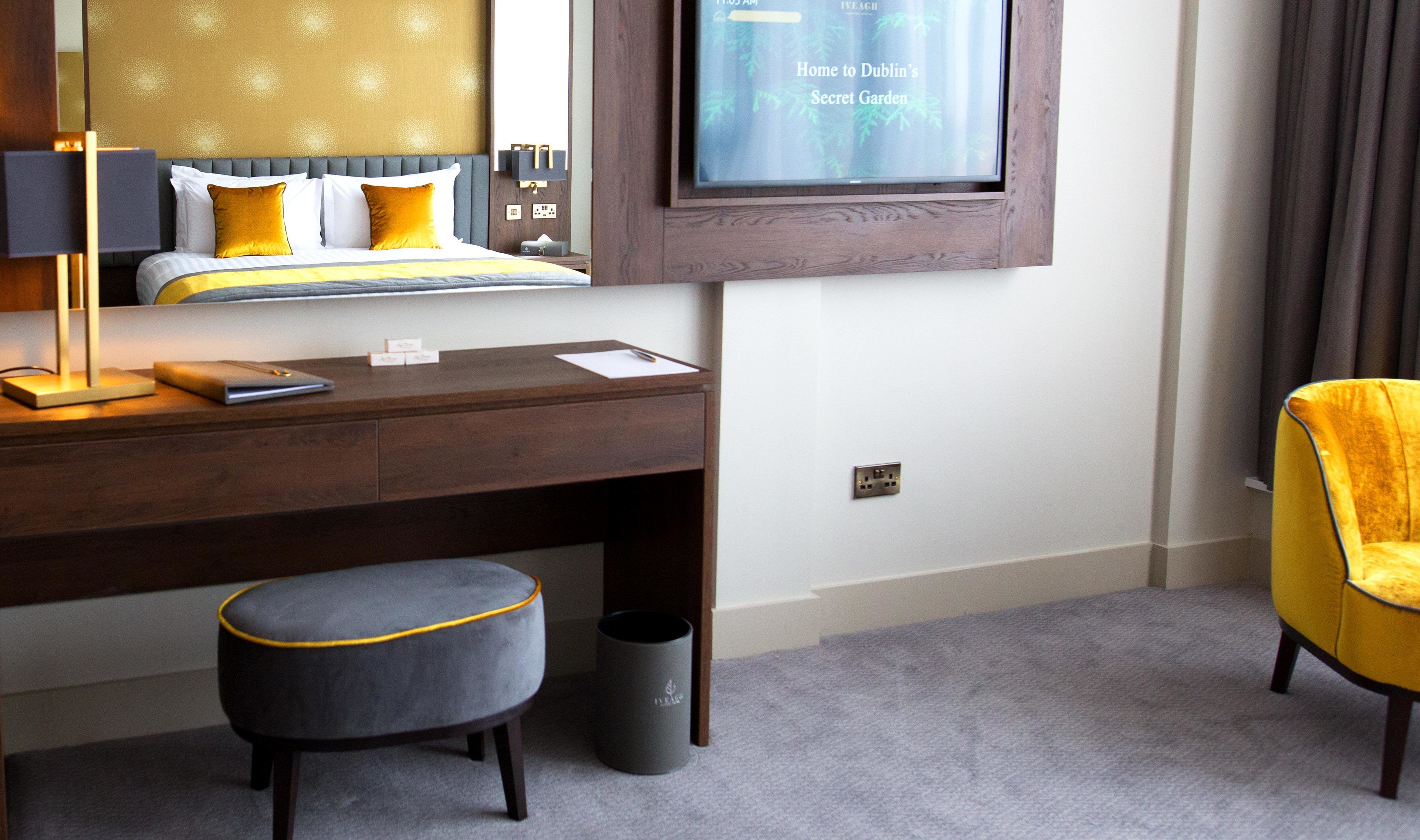 A hotel room with a bed, a desk, a chair, a TV, and a trash can.