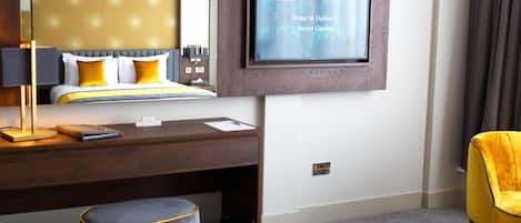 A hotel room with a bed, a desk, a chair, a TV, and a trash can.