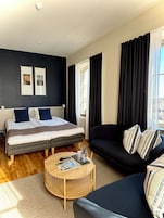 Un dormitorio moderno con una cama, un sofá, una mesita de café y una ventana con cortinas.
