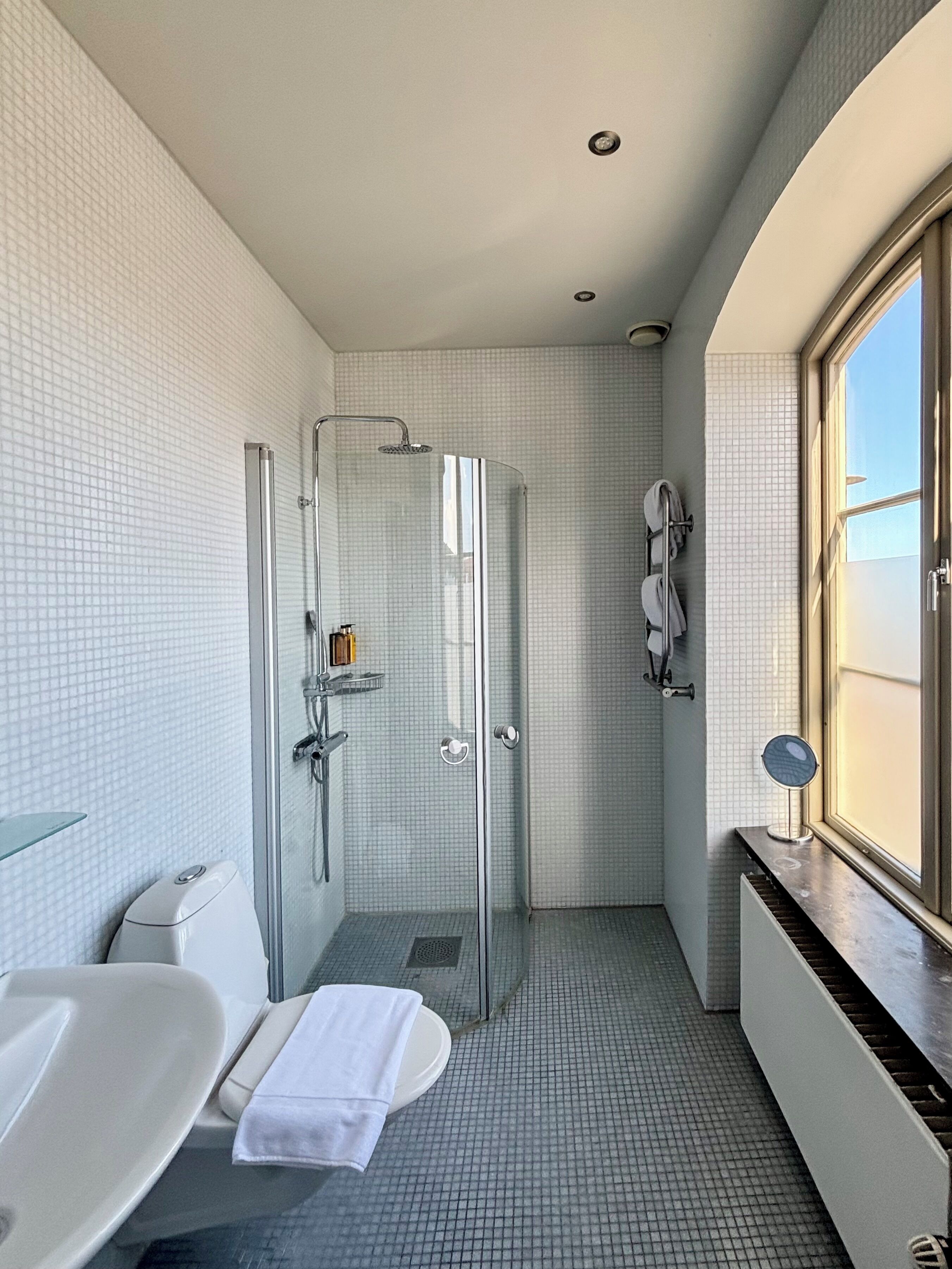 Un bagno moderno con doccia vetrata, una vasca da bagno bianca e una finestra che lascia entrare la luce naturale.