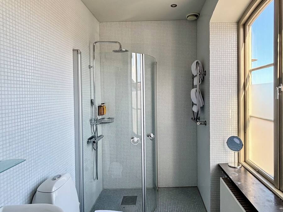 Un bagno moderno con doccia vetrata, una vasca da bagno bianca e una finestra che lascia entrare la luce naturale.