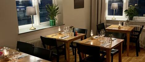 A dining area with wooden tables and chairs, potted plants, and a view of the city at night.